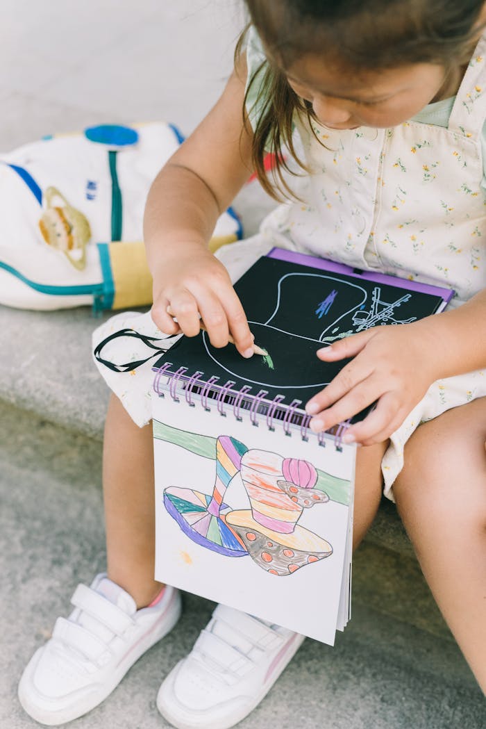 A young girl coloring in a sketchbook while sitting outside on a sunny day.